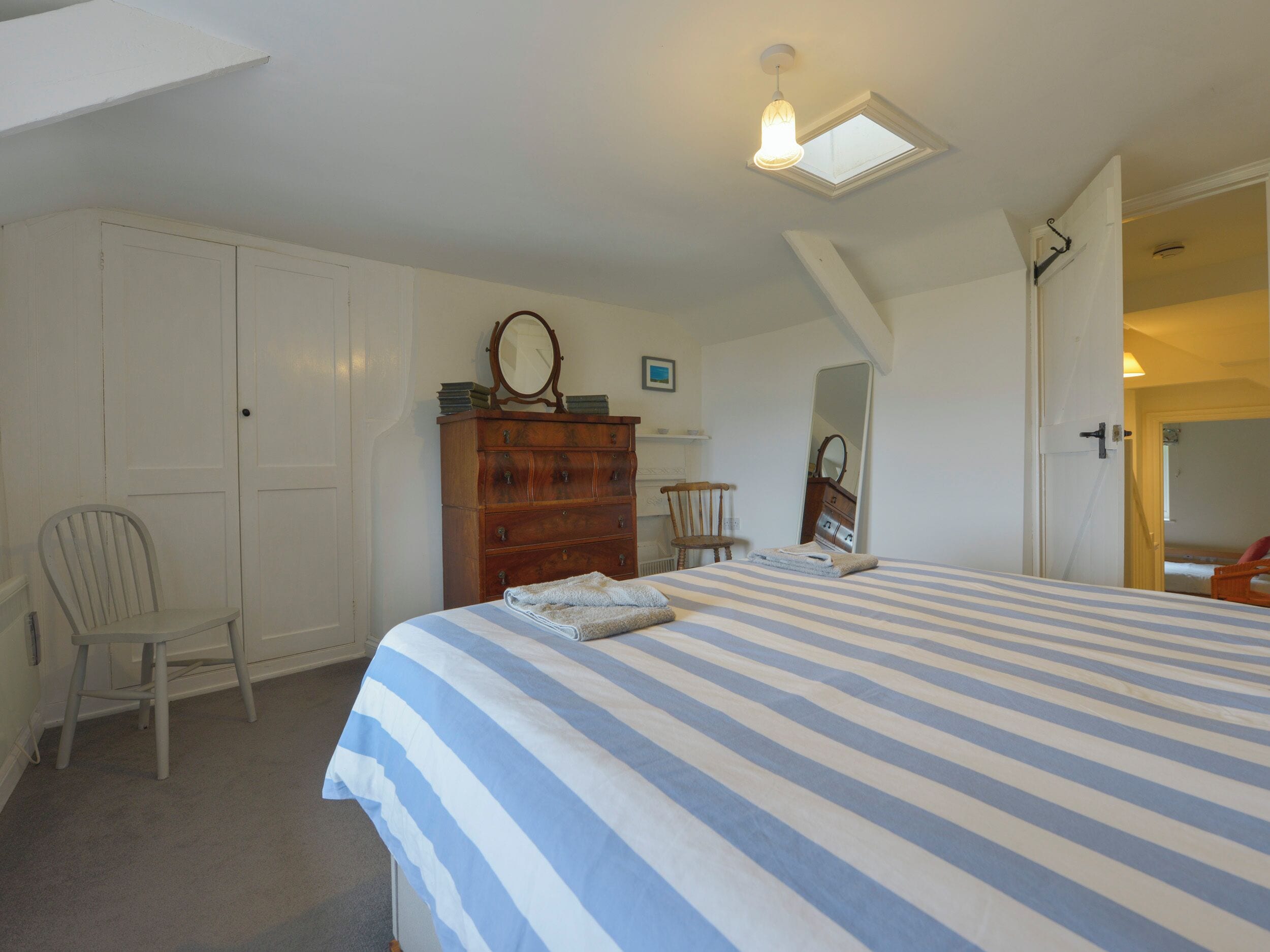 A bedroom with a large bed, a wooden dresser, a chair, and a skylight.