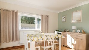 A dining area with a table and chairs, a window with curtains, a wooden cabinet, and a mirror on the wall. - Lower Brambleside (Truro)