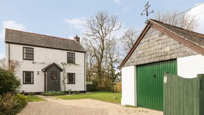 A two-story white house with a green door and a small attached garage. - Thrushel Cottage (Lifton)