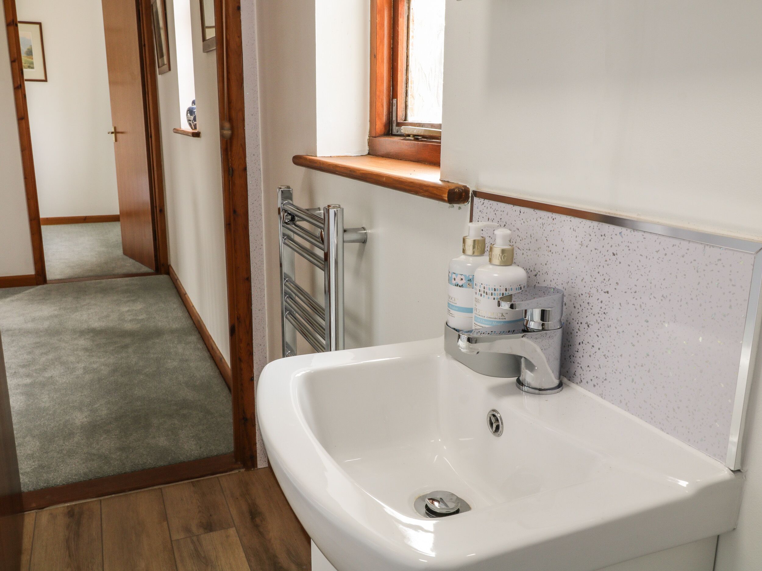 Un bagno con un lavandino bianco, un porta asciugamani e una finestra sopra il lavandino.