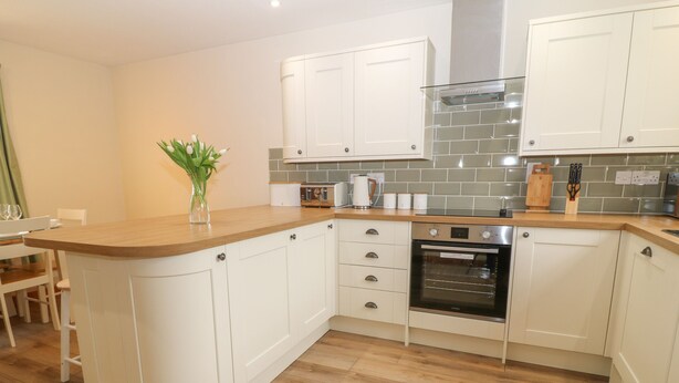 A modern kitchen with white cabinets, a wooden countertop, and a built-in oven. - Thrushel Cottage (Lifton)