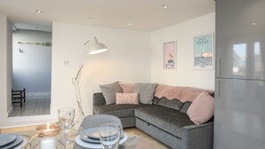 Un salon moderne avec un canapé gris, une table à manger dressée avec des assiettes et des verres, un lampadaire et un réfrigérateur.