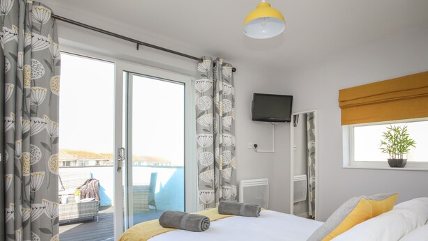 Une chambre à coucher avec un lit, une télévision, une fenêtre avec une plante et une vue sur un immeuble et l’eau à l’extérieur.