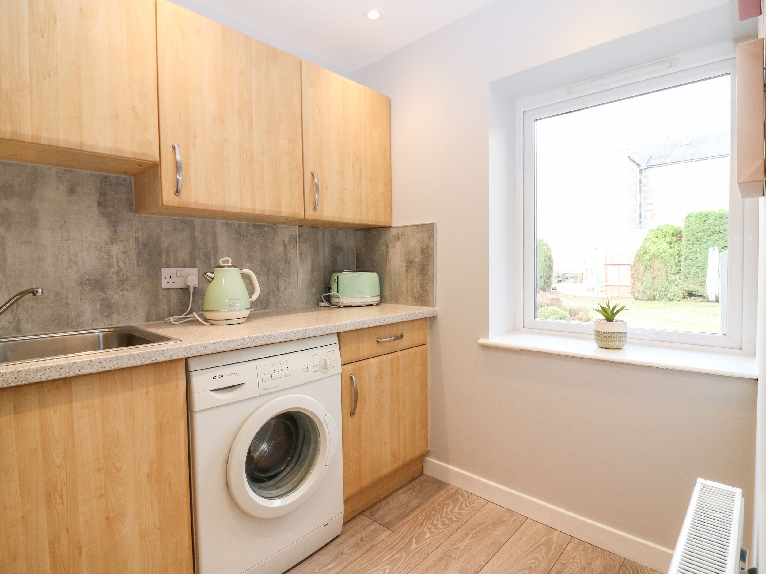 A compact kitchen with wooden cabinets, a washing machine, a kettle, and a toaster.
