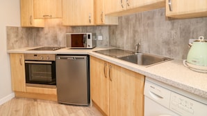 A modern kitchen with wooden cabinets, a stainless steel sink, a microwave, an oven, and a dishwasher. - Gairnlea Cottage (Ballater)