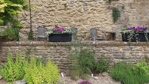 A stone wall with three wicker chairs and black flower planters. - Jasmine Cottage (Beaminster)