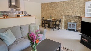A modern living room with a sofa, a coffee table, and a dining area with a stone wall and a fireplace. - Jasmine Cottage (Beaminster)