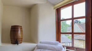 A corner of a room with a wooden barrel, a stack of white towels, and a window with a view of houses. - Jasmine Cottage (Beaminster)