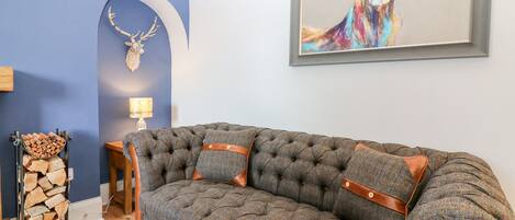 A tufted grey sofa with leather accents, a mounted deer head, and a colorful deer painting.