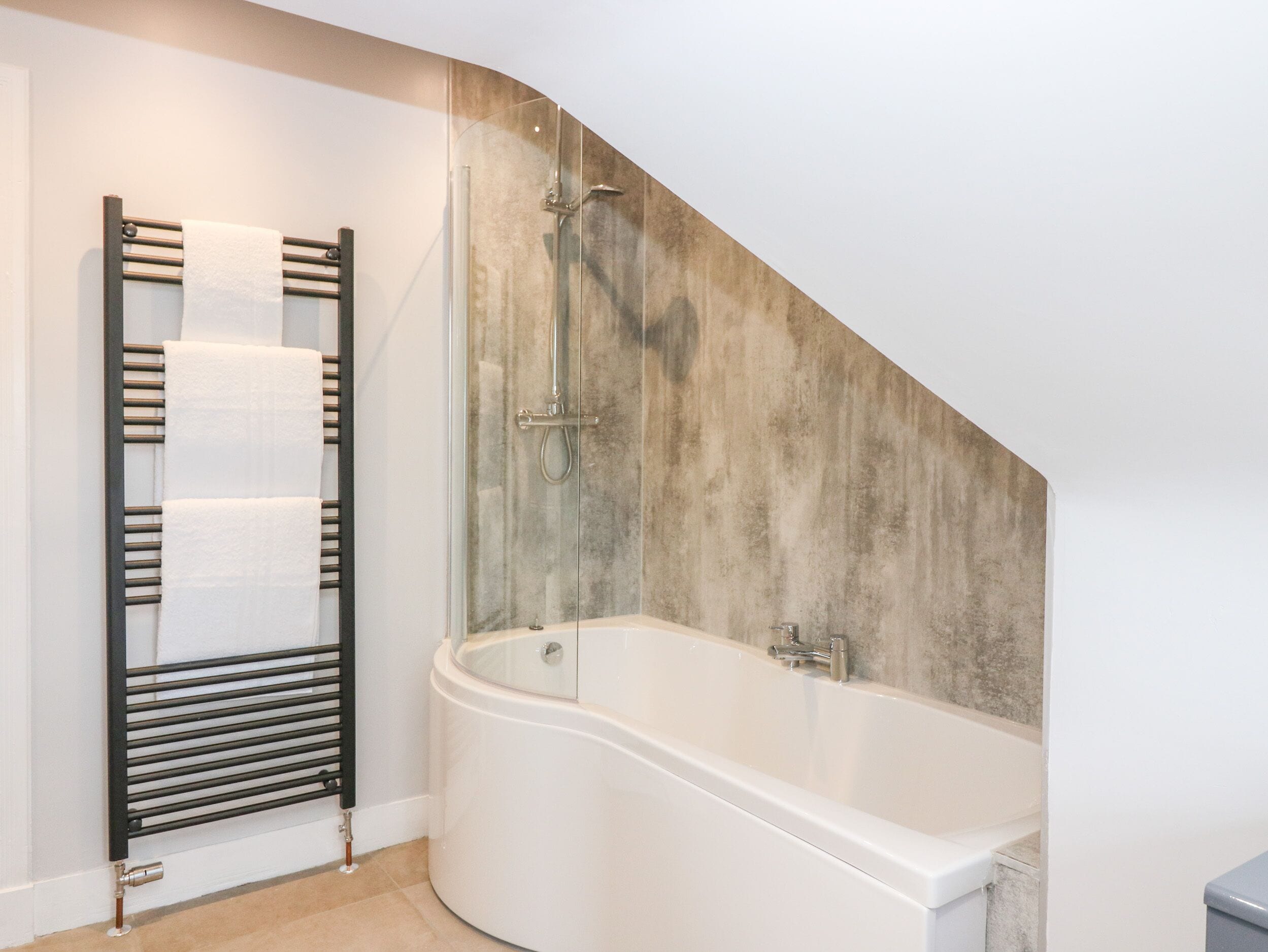 A modern bathroom with a freestanding bathtub, a glass-enclosed shower, and a towel rack with multiple towels.