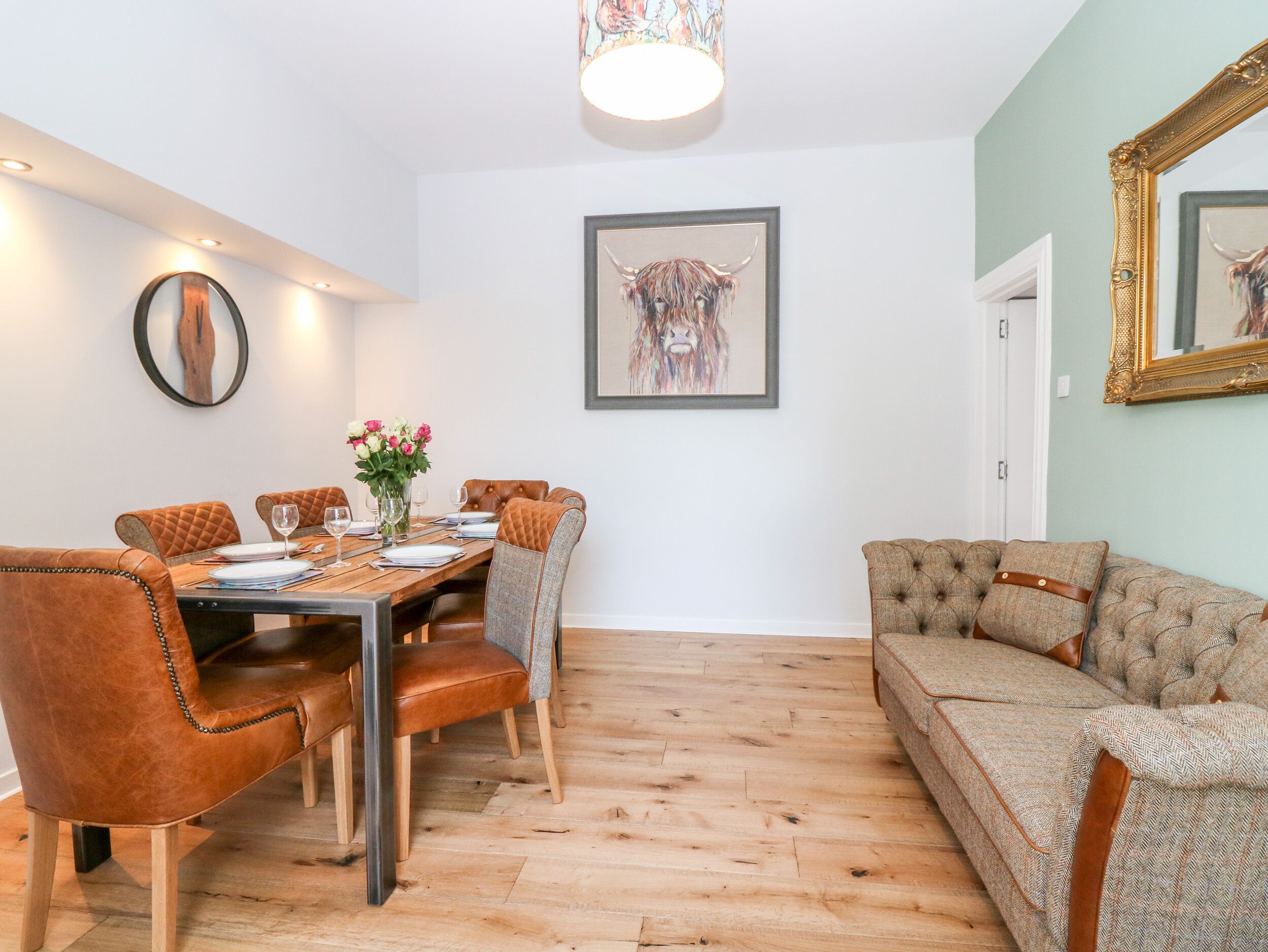 Un coin repas avec une table en bois dressée pour six personnes, entourée de chaises en cuir. Une grande œuvre d’art encadrée représentant un taureau est accrochée au mur, au-dessus de la table.