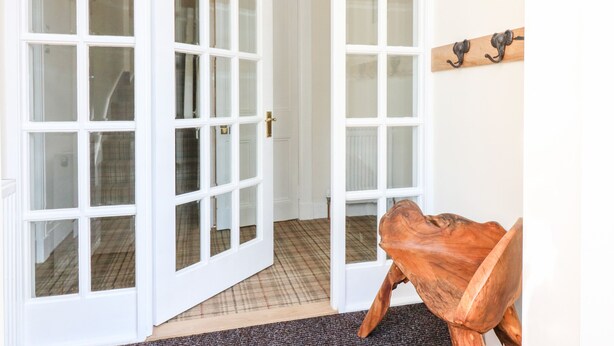 A hallway with white double doors, a wooden coat rack, and a sign on the wall. - Gairnlea House (Ballater)