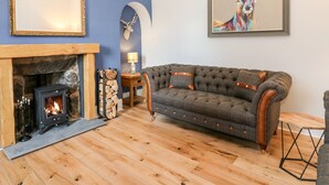 A cozy living room with a fireplace, a sofa, and a painting of a deer. - Gairnlea House (Ballater)