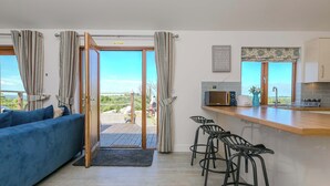 A modern living room with a blue sofa, a wooden coffee table, and a kitchen area with a microwave and bar stools. - Mellydonen Beder Del , Tor Down Quarry (Bodmin)