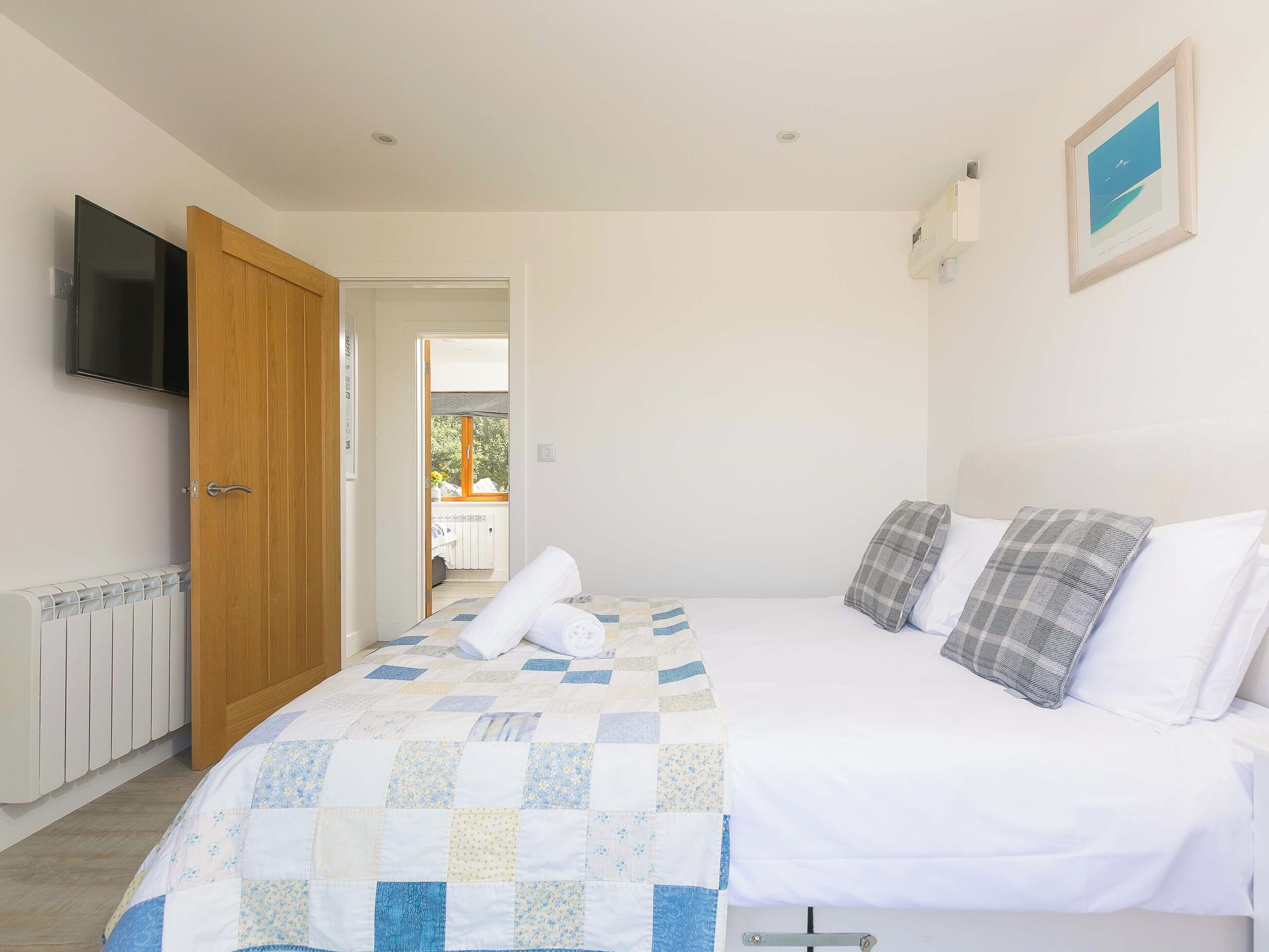 A bedroom with a bed, a television, a door, and a view to an outdoor balcony.