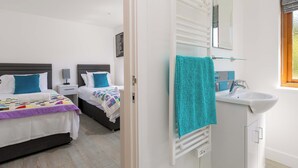 A bedroom with two beds, a bathroom with a sink and mirror, and a window with a view. - Mellydonen Beder Del , Tor Down Quarry (Bodmin)