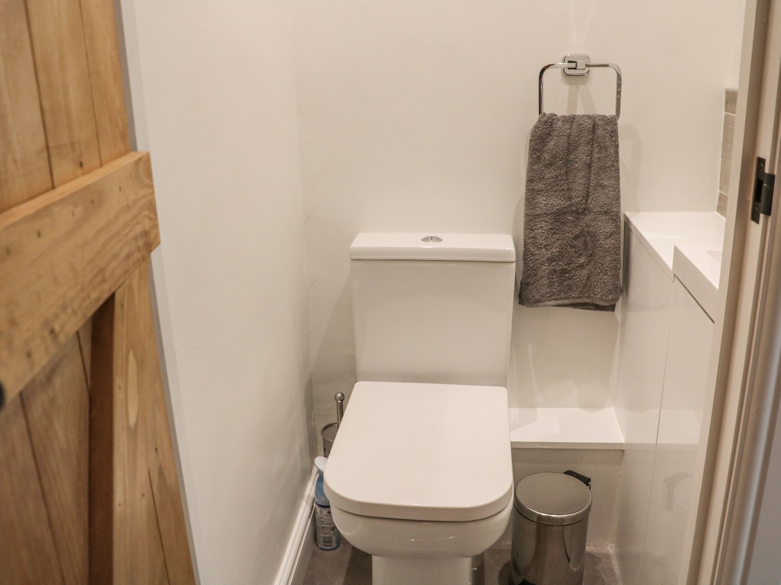 Une petite salle de bain avec des toilettes blanches, une petite poubelle et une serviette suspendue à un porte-serviettes.