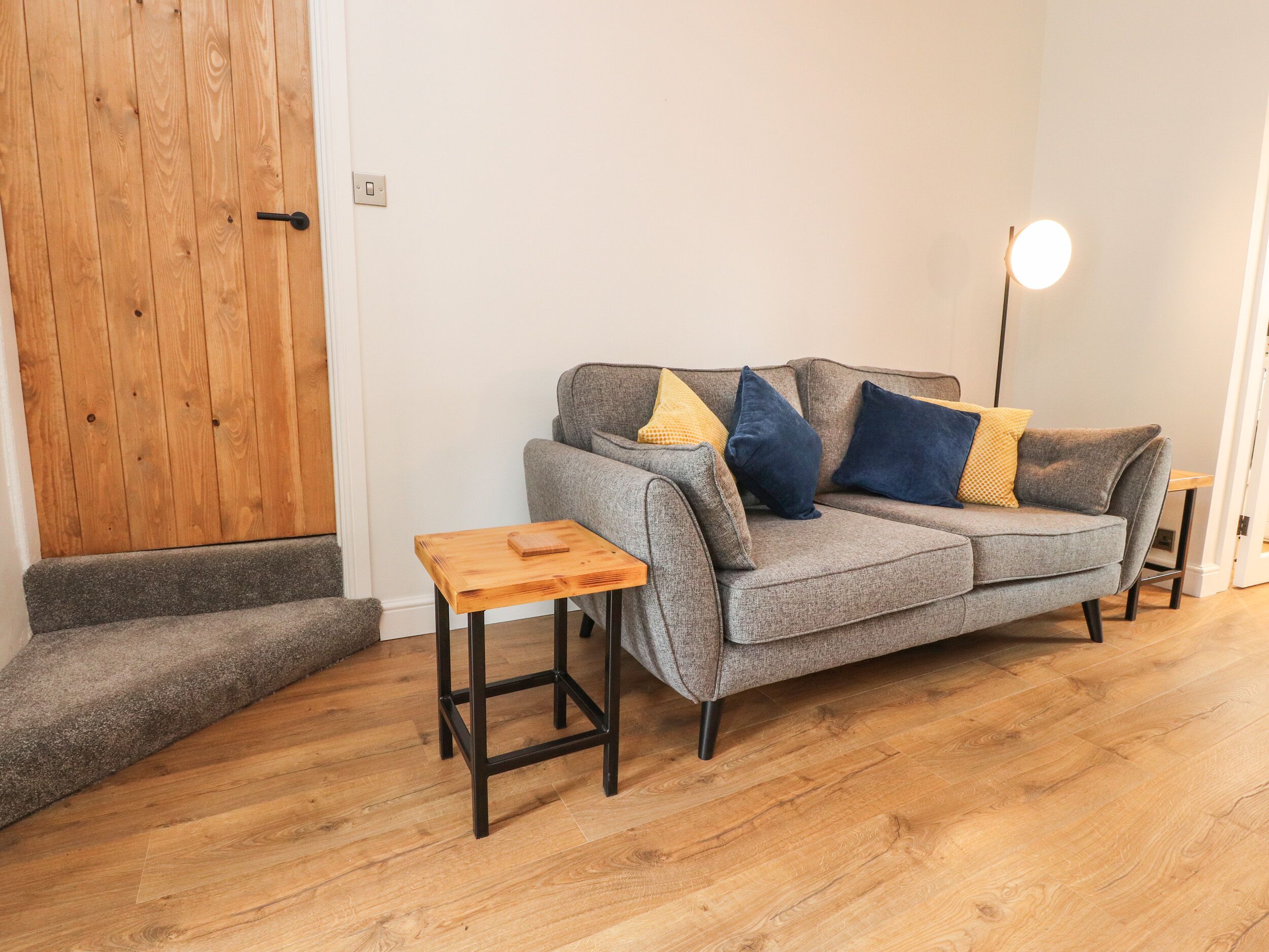 Una sala de estar con un sofá gris, una mesita de madera y un taburete pequeño de madera.