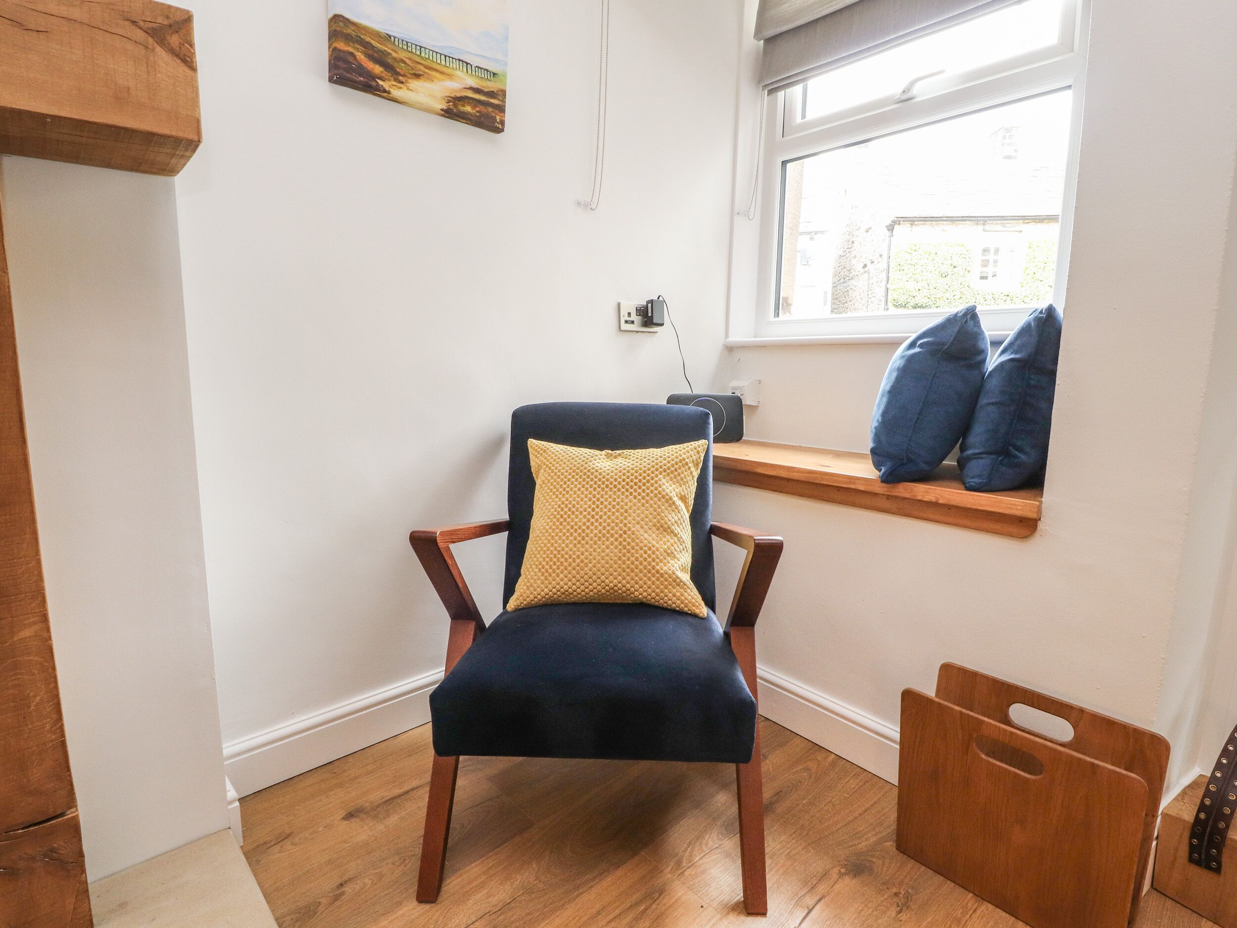 Une chaise avec un coussin jaune, un banc en bois avec des coussins bleus et une fenêtre donnant sur des immeubles.