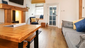 A cozy room with a wooden table, a blue chair, a grey sofa, and a television mounted on the wall.