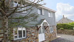 Une maison à deux étages avec une façade en pierre, une porte blanche et un petit porche agrémenté d’une lanterne.