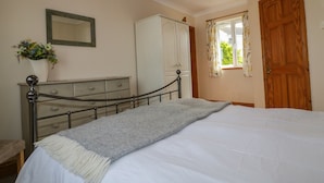 Une chambre à coucher avec un lit, une commode, un miroir et une fenêtre avec des rideaux.