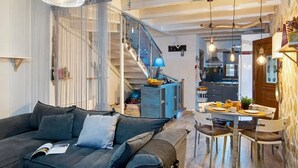 A modern living room with a dark sofa, a dining table with chairs, a staircase, and a kitchen area. - hara luxury house (Gaios)