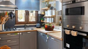 A modern kitchen with grey cabinets, a built-in oven, and a window providing natural light. - hara luxury house (Gaios)