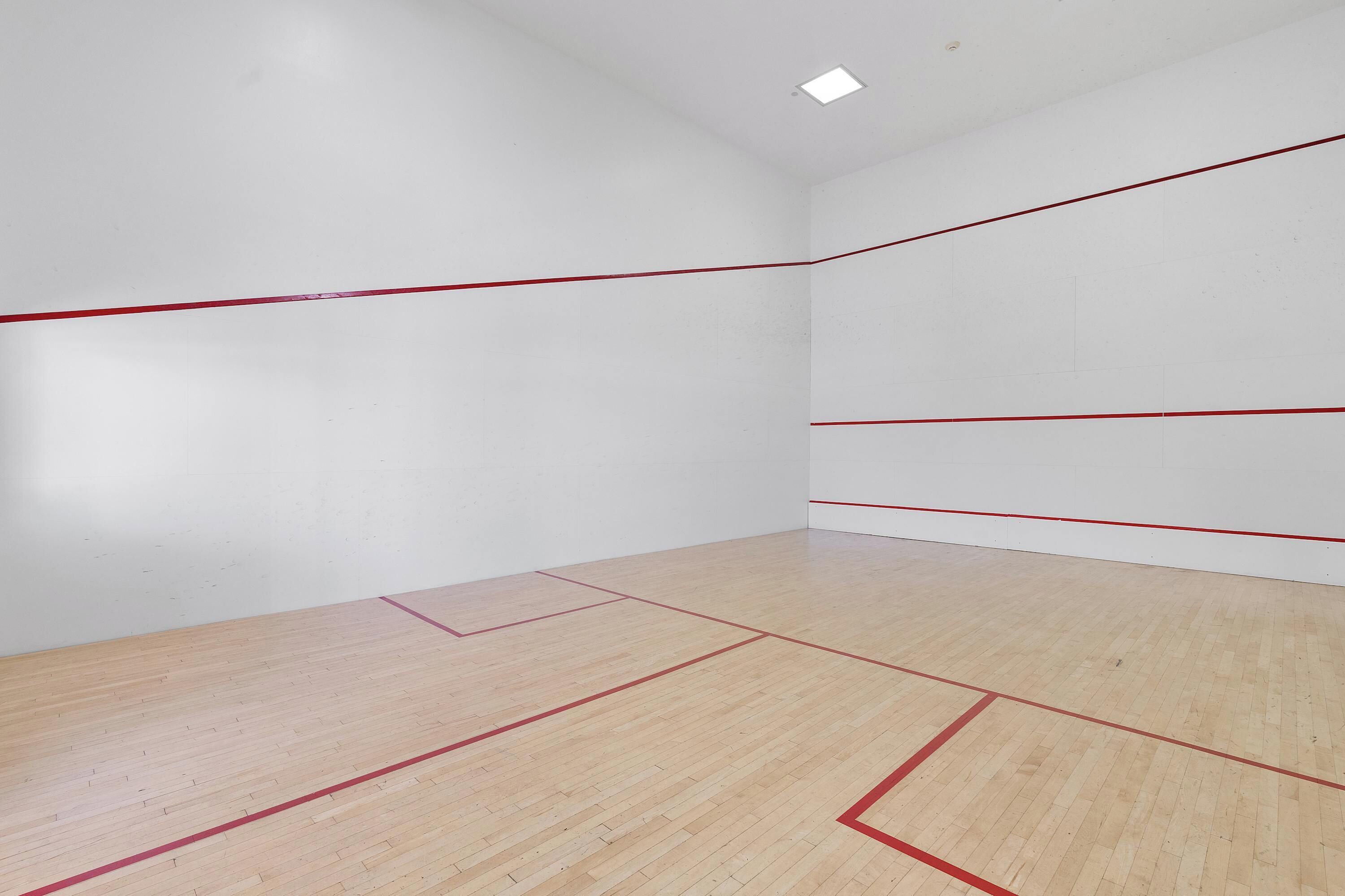 Ein Squashplatz mit weißen Wänden und einem mit roten Linien markierten Holzboden.