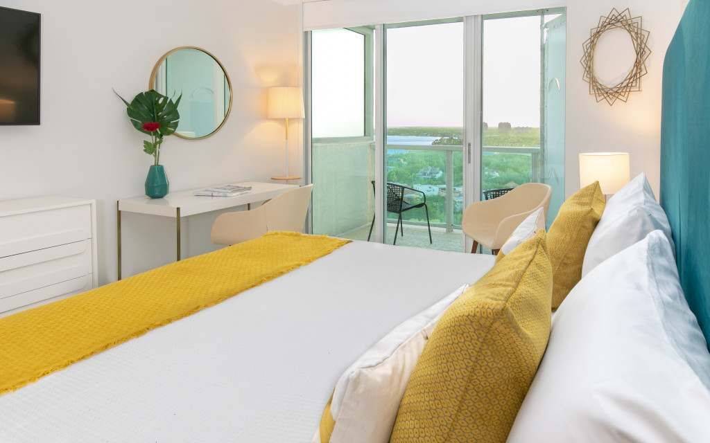 A hotel room with a bed, a desk, a chair, and a balcony with a view.