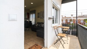Balcón abierto con mesa y sillas de comedor, un sofá en la habitación contigua y vista al vecindario.