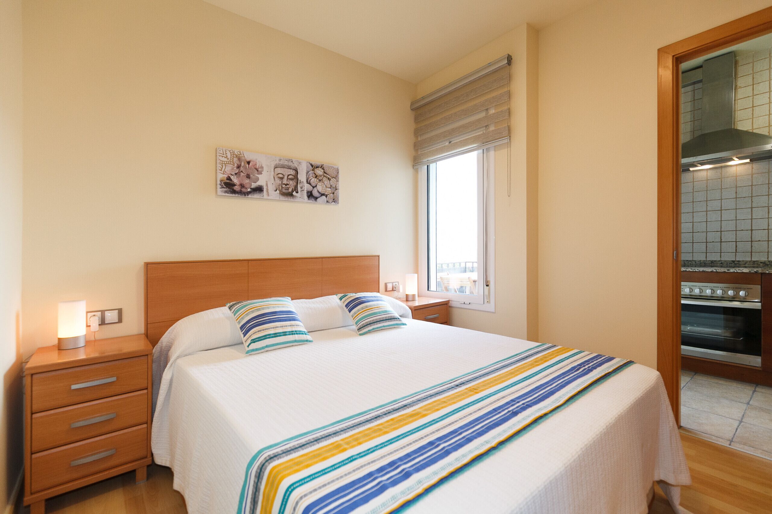 Une chambre avec un lit, une table de chevet, une fenêtre et un coin cuisine.