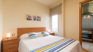 Un dormitorio con cama, mesita de noche, ventana y una zona de cocina.