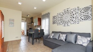 Una sala de estar con un sofá gris, una mesa de comedor con sillas y una cocina al fondo.