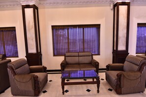 A room with striped armchairs, a glass coffee table, and a large window with blinds. - Simsan Hotel (Chennai)