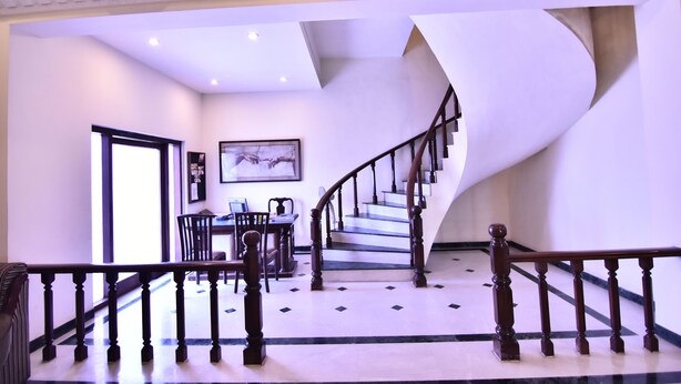 Un interior moderno con una escalera curva, un comedor con mesa y sillas, y una obra de arte enmarcada en la pared.