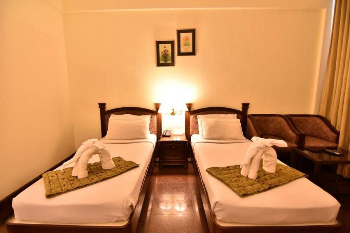 A hotel room with two single beds, a nightstand with a lamp, and a chair.