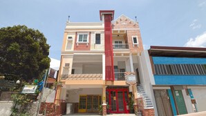 Um edifício com vários andares, apresentando uma característica vermelha vertical central, uma varanda e uma entrada no nível da rua com porta vermelha.