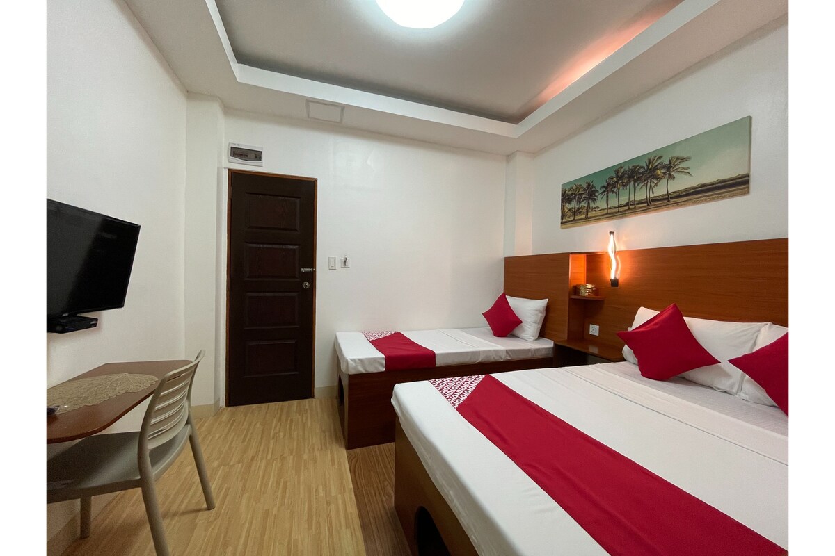 A hotel room with two beds, a TV, a desk, and a painting on the wall.