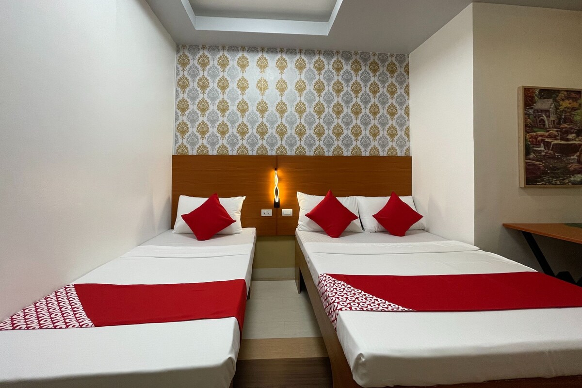 Hotellihuone, jossa on kaksi sänkyä, puinen pääty, kuvioitu tapetti ja taulu seinällä.