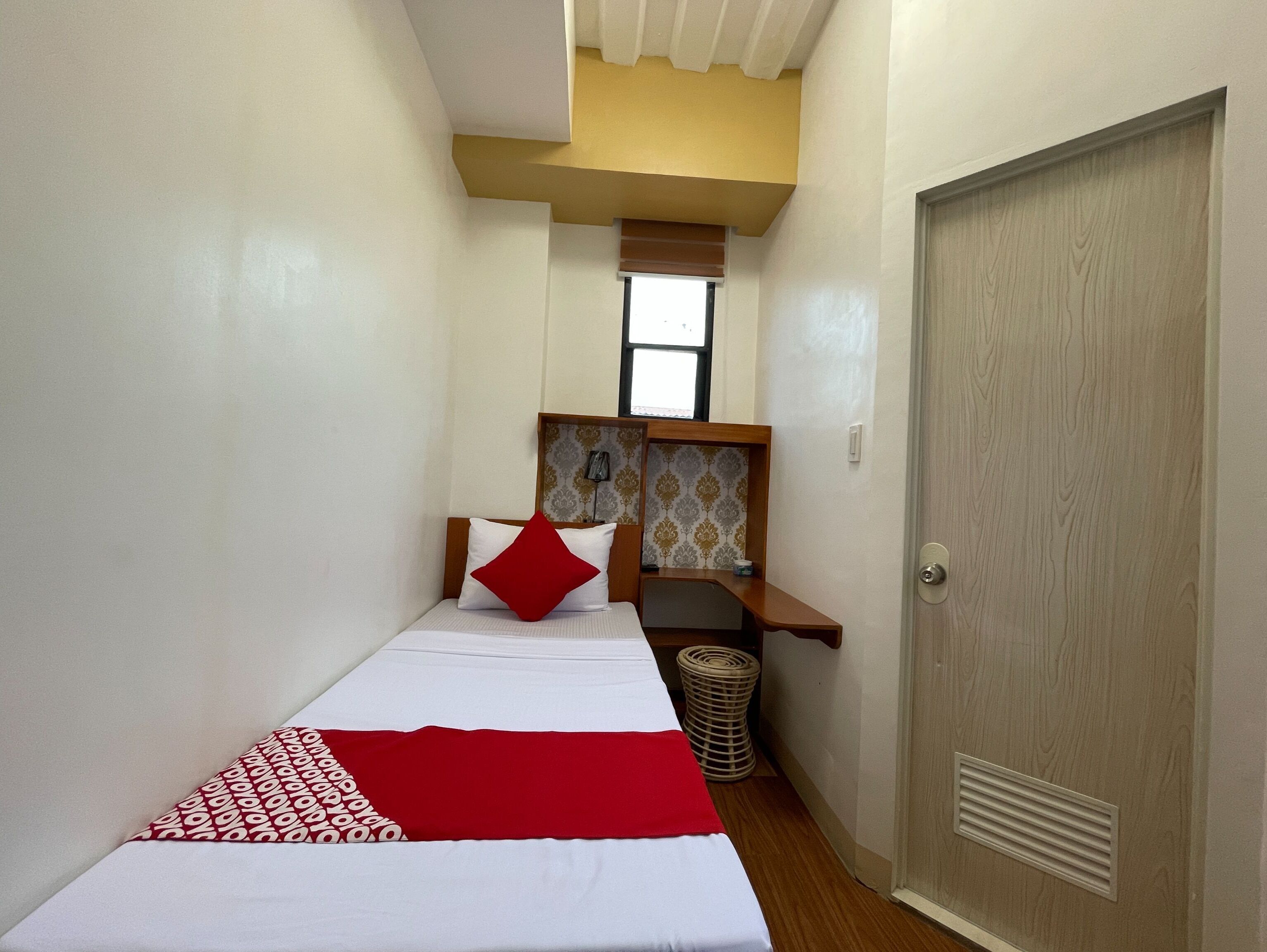 A narrow room with a bed, a small desk, and a door.