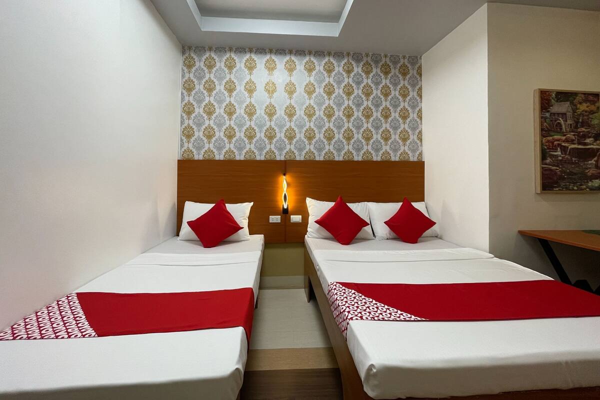 Een hotelkamer met twee bedden, een houten hoofdbord, behang met een patroon en een schilderij aan de muur.