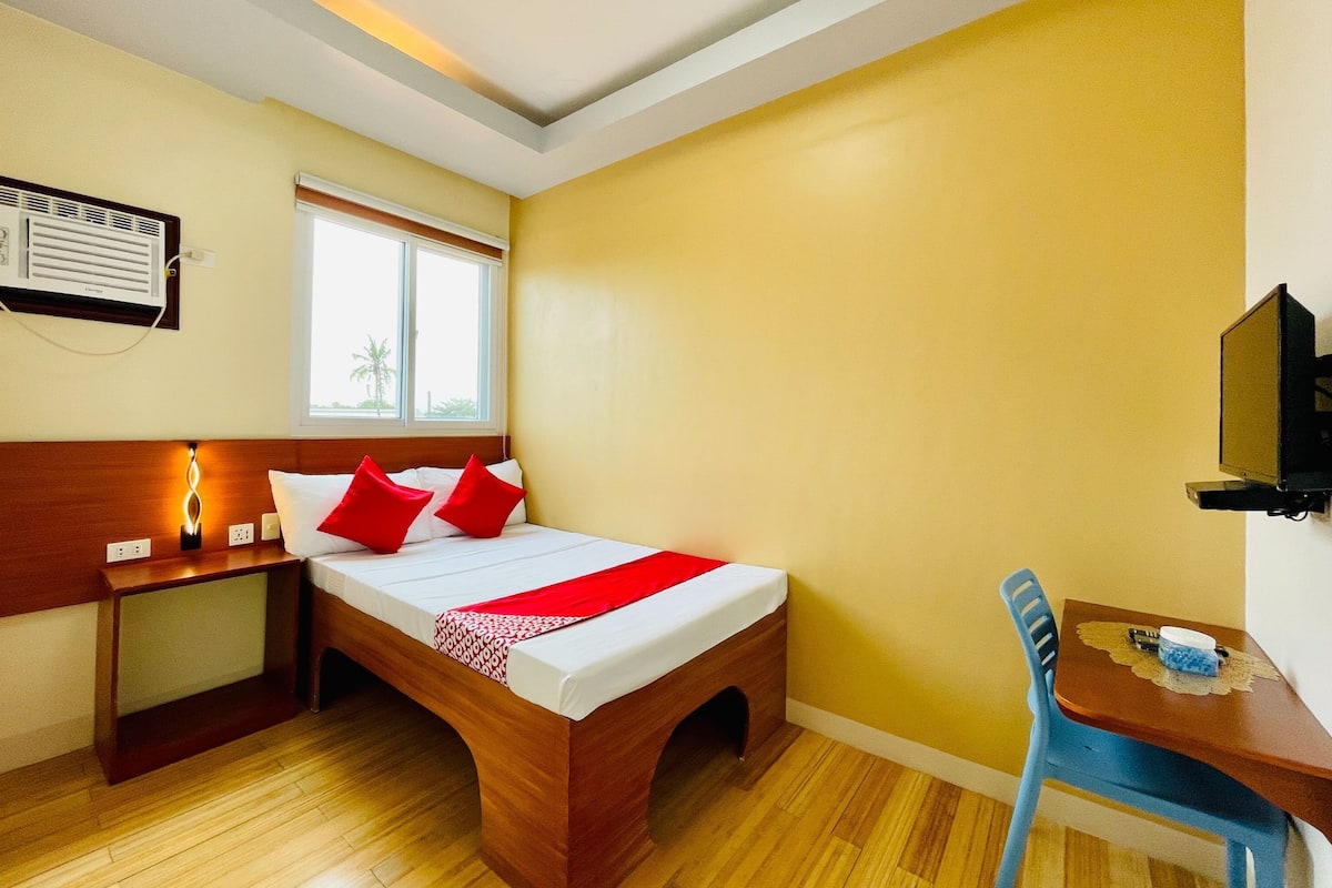 Een hotelkamer met een houten bed, een nachtkastje met een lamp, een raam met uitzicht, een televisie en een bureau met een stoel.