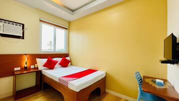 A hotel room with a wooden bed, a bedside table with a lamp, a window with a view, a TV, and a desk with a chair.