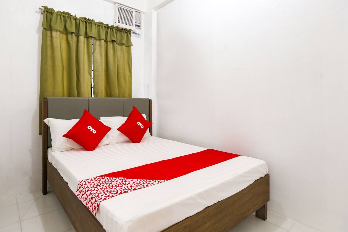 A neatly made bed with a white and red bedspread, two red pillows with "OYO" text, and green curtains.
