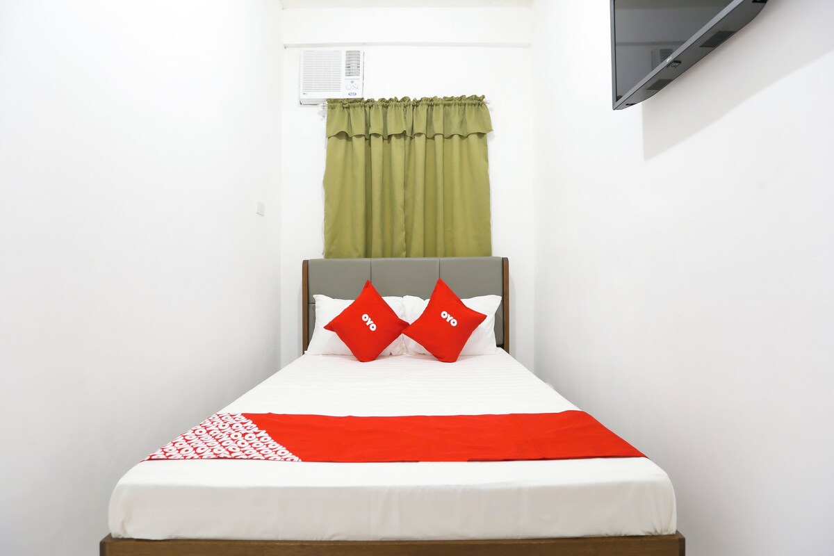A single bed with a grey headboard, white bedding, and two red pillows.
