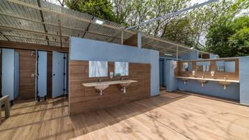 Un baño público con paredes de madera, varios lavamanos y techo metálico.
