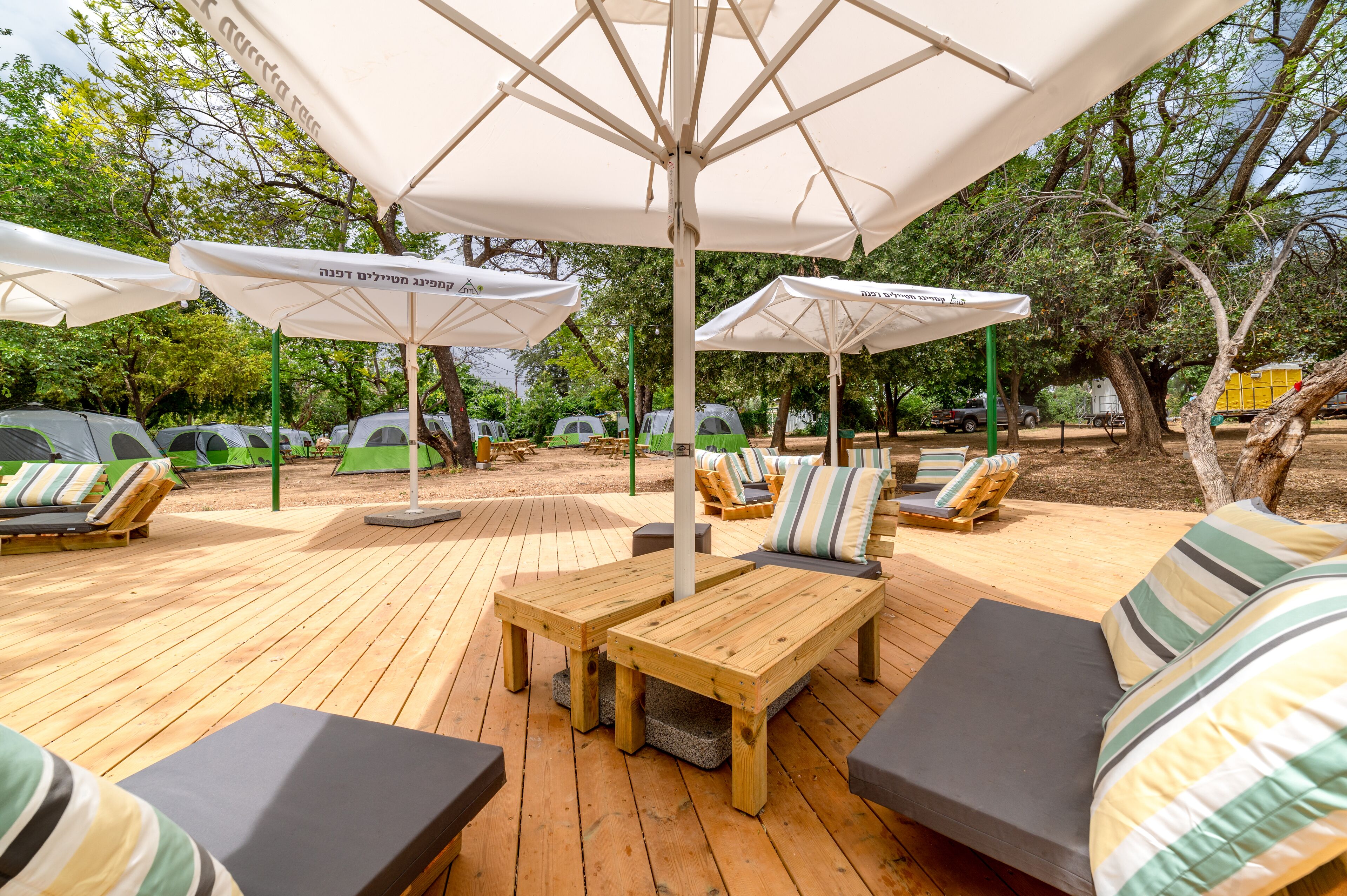 A wooden deck with outdoor seating, including lounge chairs and tables, under large umbrellas.