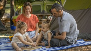 A family of three sitting on a striped mat outdoors with a tent in the background. - Camping Dafna - By Travel Hotel Chain (HaGalil HaElyon)
