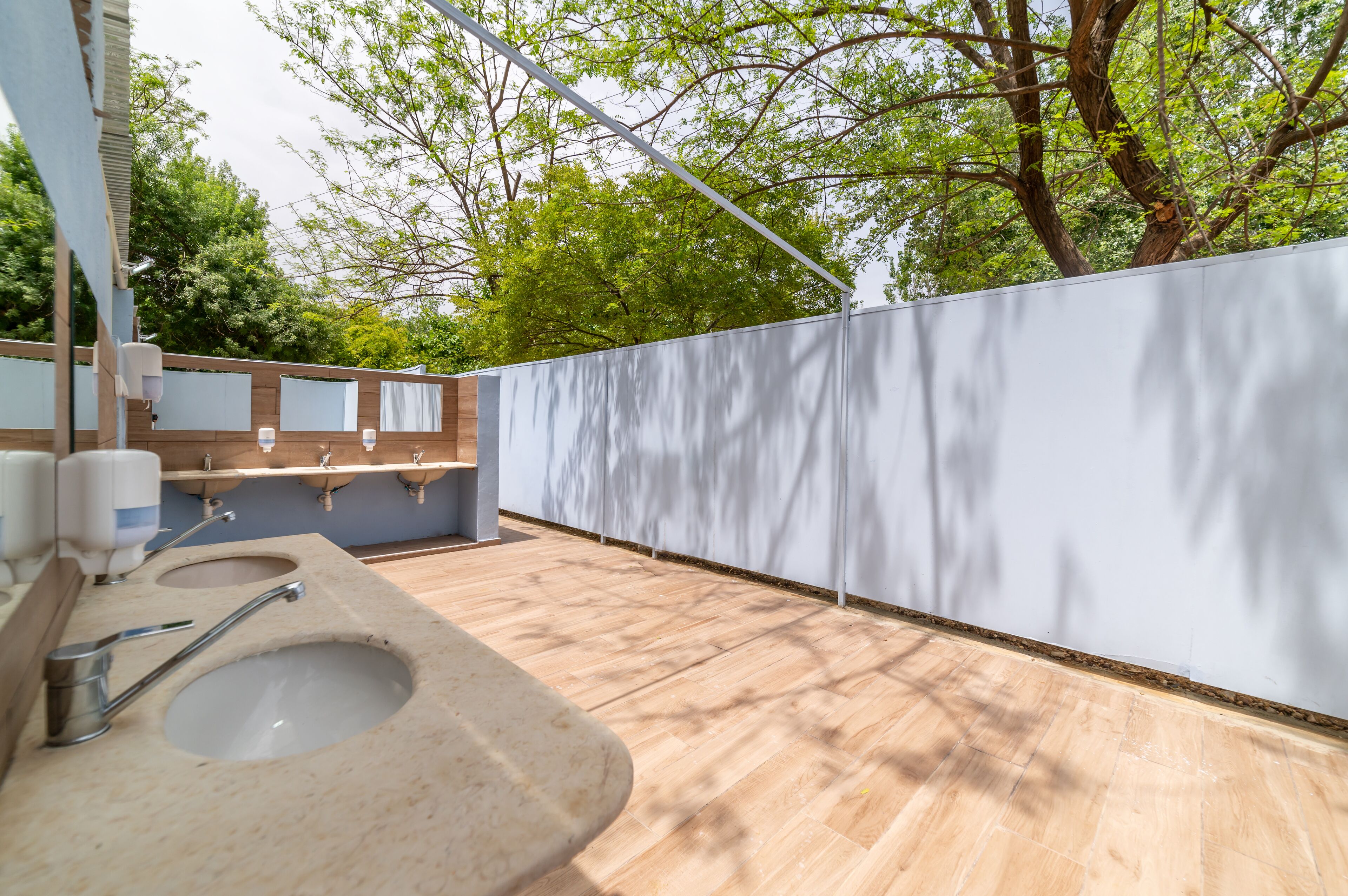 Un bagno esterno moderno con pavimento in legno, un lavandino grande e un pannello divisorio bianco.